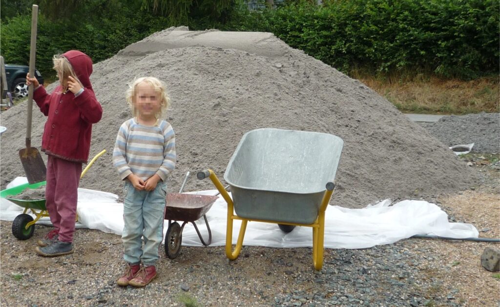 Sandtransport mit einer Schubkarre im Naturgarten – körperliche Aktivität, Gartenarbeit ohne Maschinen, Bewegung im Alltag, Selbstwirksamkeit und naturnahe Lebensgestaltung für Kinder