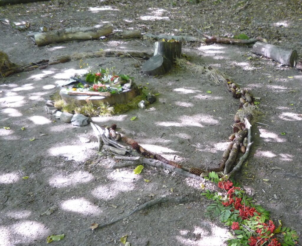 Land-Art-Gestaltung auf dem Waldboden aus Vogelbeeren, Zapfen, Stöcken, Moos und Steinen als kreative Naturerfahrung und entspannende Tätigkeit im Wald.
